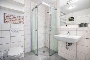 Un baño moderno con ducha de vidrio, lavamanos blanco y retrete.