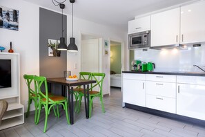 Cozinha moderna com armários brancos, área de jantar com cadeiras verdes e uma TV de tela plana.