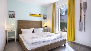 Une chambre d’hôtel avec un lit, une table de chevet, une lampe, des œuvres d’art au mur et une fenêtre avec des rideaux.