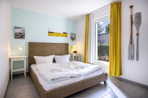 Una habitación de hotel con una cama, una mesita de noche, una lámpara, obras de arte en la pared y una ventana con cortinas.