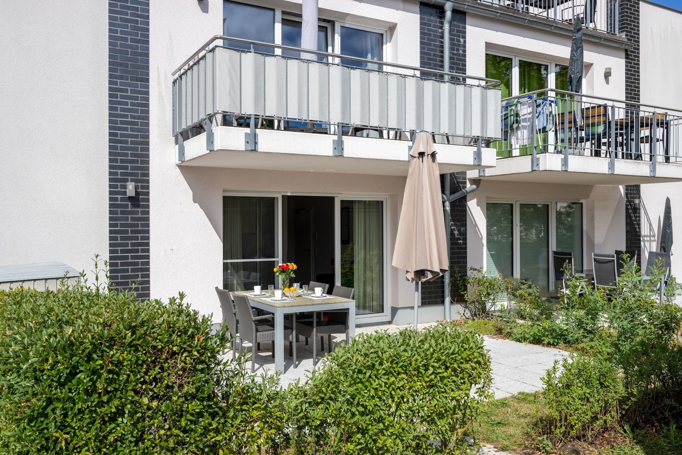 Un bâtiment moderne à deux étages doté d’un balcon, d’un espace extérieur aménagé pour s’asseoir et d’un jardin.