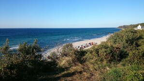 Une plage bordée d’une rangée de cabanes de plage aux couleurs vives, une mer d’un bleu limpide et, au loin, un bâtiment blanc.