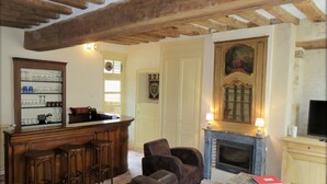 A cozy living room with a fireplace, a bar area with stools, and a comfortable seating arrangement. - Historic 18th Century Home with Modern Comforts in Medieval Village (Montmirail)