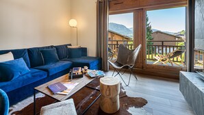 Un salon chaleureux avec un canapé bleu, une table basse en bois et une vue sur un paysage montagneux, visible à travers de grandes portes-fenêtres coulissantes.