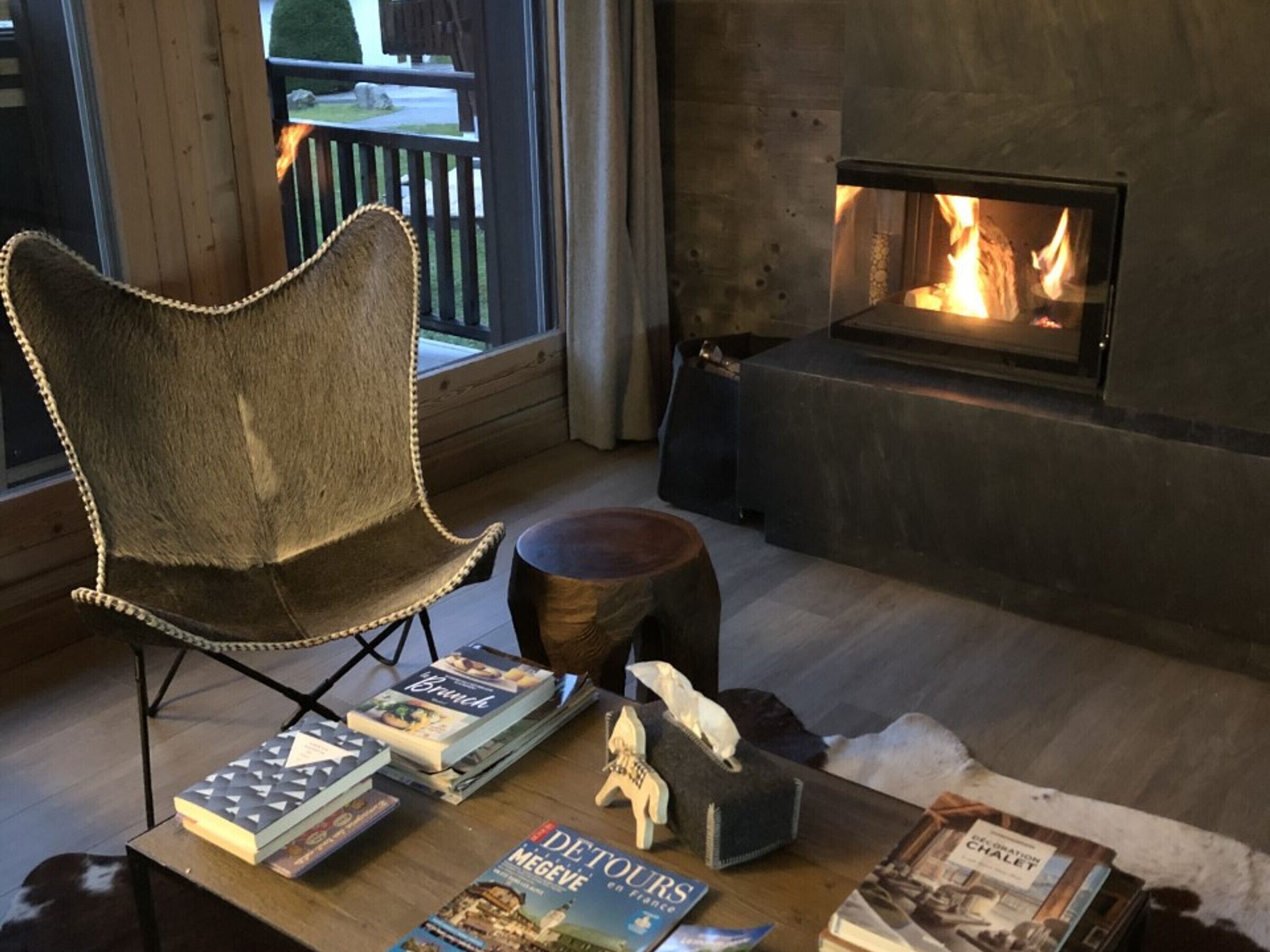 A cozy living room with a fireplace, a plush chair, and a coffee table with books and a decorative item.