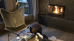 Un salon chaleureux avec une cheminée, un fauteuil confortable et une table basse agrémentée de livres et d’un objet décoratif.