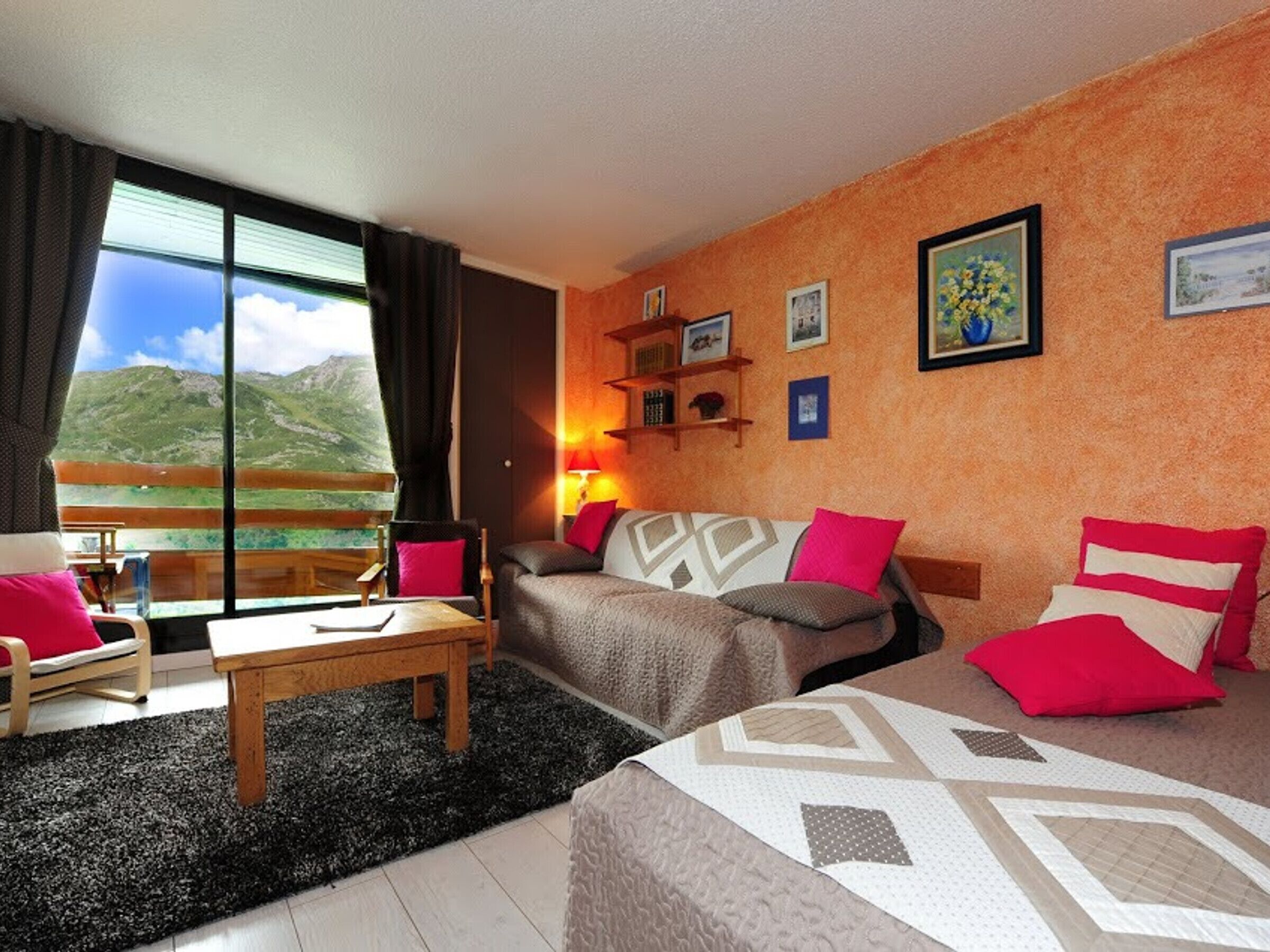 A hotel room with a large window offering a mountain view, a sofa, a chair, a small table, and a lamp.