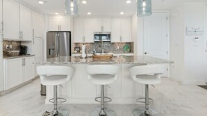 Une cuisine moderne avec des meubles blancs, un plan de travail en granit, des appareils électroménagers en acier inoxydable et trois tabourets de bar.