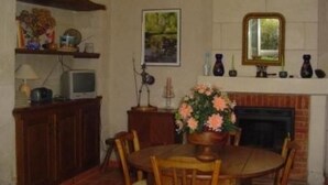 A dining room with a fireplace, a table with chairs, a television on a cabinet, and a framed picture on the wall.