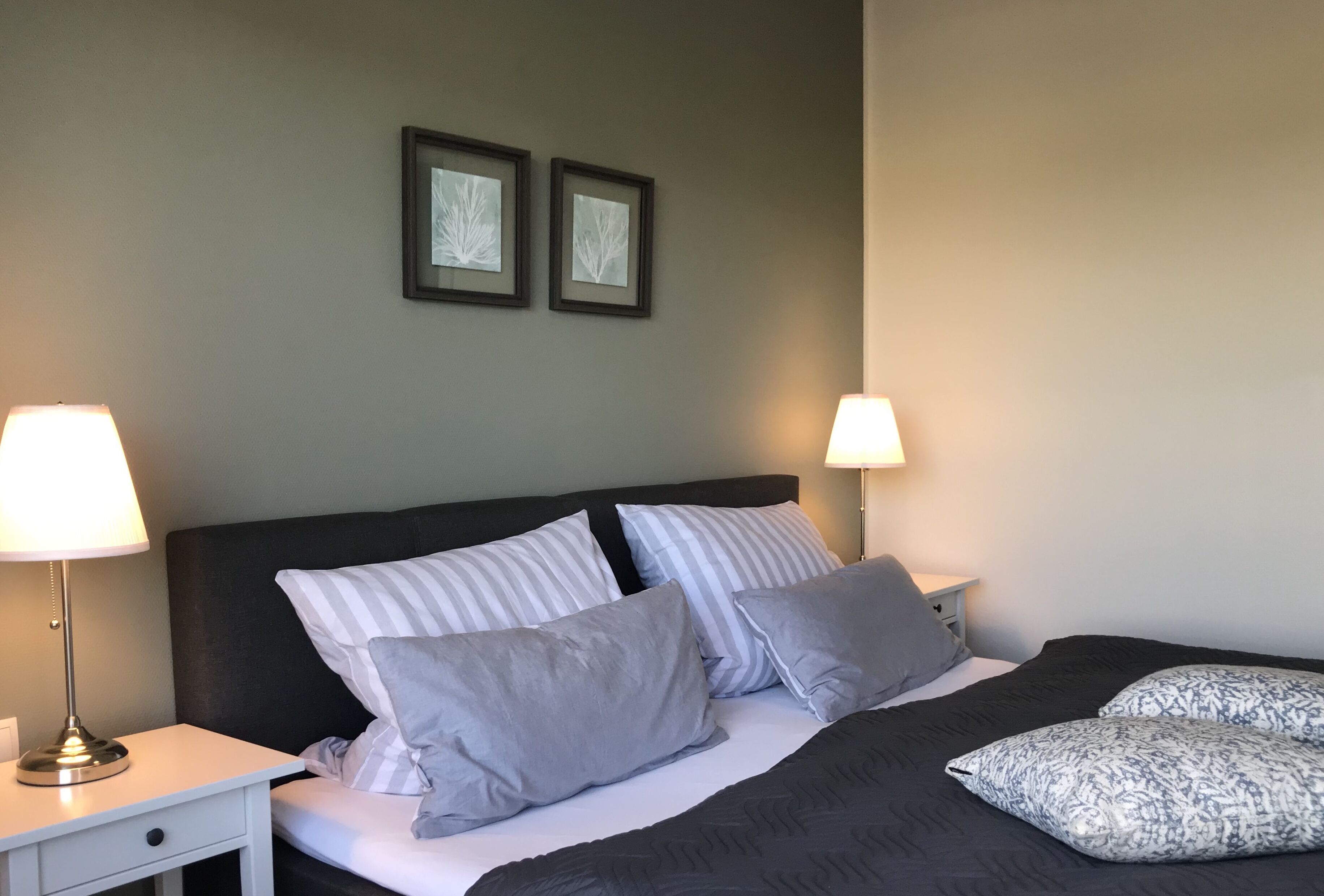 A neatly made bed with striped and solid pillows, two bedside lamps, and framed artwork on the wall.