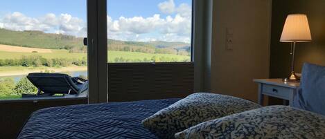 Een hotelkamer met een groot raam dat uitzicht biedt op een groen landschap en een stoel bij het raam.