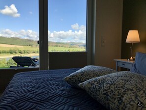 Une chambre d’hôtel dotée d’une grande fenêtre donnant sur un paysage verdoyant, avec un fauteuil placé près de la fenêtre.