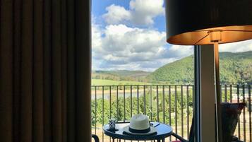 A balcony with a view of a river and hills, a table with a hat, and a lamp.