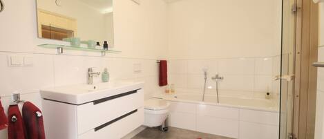 A modern bathroom with a glass shower enclosure, a white vanity with a mirror, and a red bath mat.