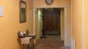 Un couloir avec une porte en bois, une horloge, un miroir et une table sur laquelle se trouvent un panier et une bougie.