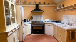 Une cuisine compacte équipée d’une cuisinière, d’un four et d’un lave-vaisselle. On y trouve des placards et des étagères au-dessus du plan de travail.