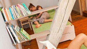 Une pièce avec un lit en mezzanine, une petite table et une bibliothèque remplie de livres.