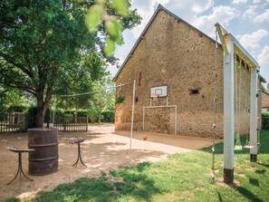 Un espace extérieur rustique comprenant un panier de basket, une table en bois et un grand tonneau.