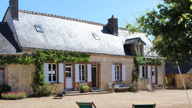 Une maison à deux étages avec une allée en gravier, un porche et deux chaises pliantes vertes.