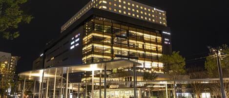 Een modern hotel met meerdere verdiepingen, een overdekte ingang en een zichtbaar treinstation op de voorgrond.