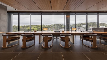 Una sala de reuniones moderna con una larga mesa y seis sillas de madera, ventanas amplias que ofrecen vistas de la ciudad y un techo de madera.