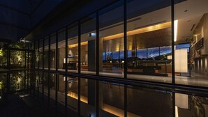 A modern hotel lobby with a glass facade, a reception area, and a view of the cityscape at dusk. - THE BLOSSOM KUMAMOTO (Kumamoto)
