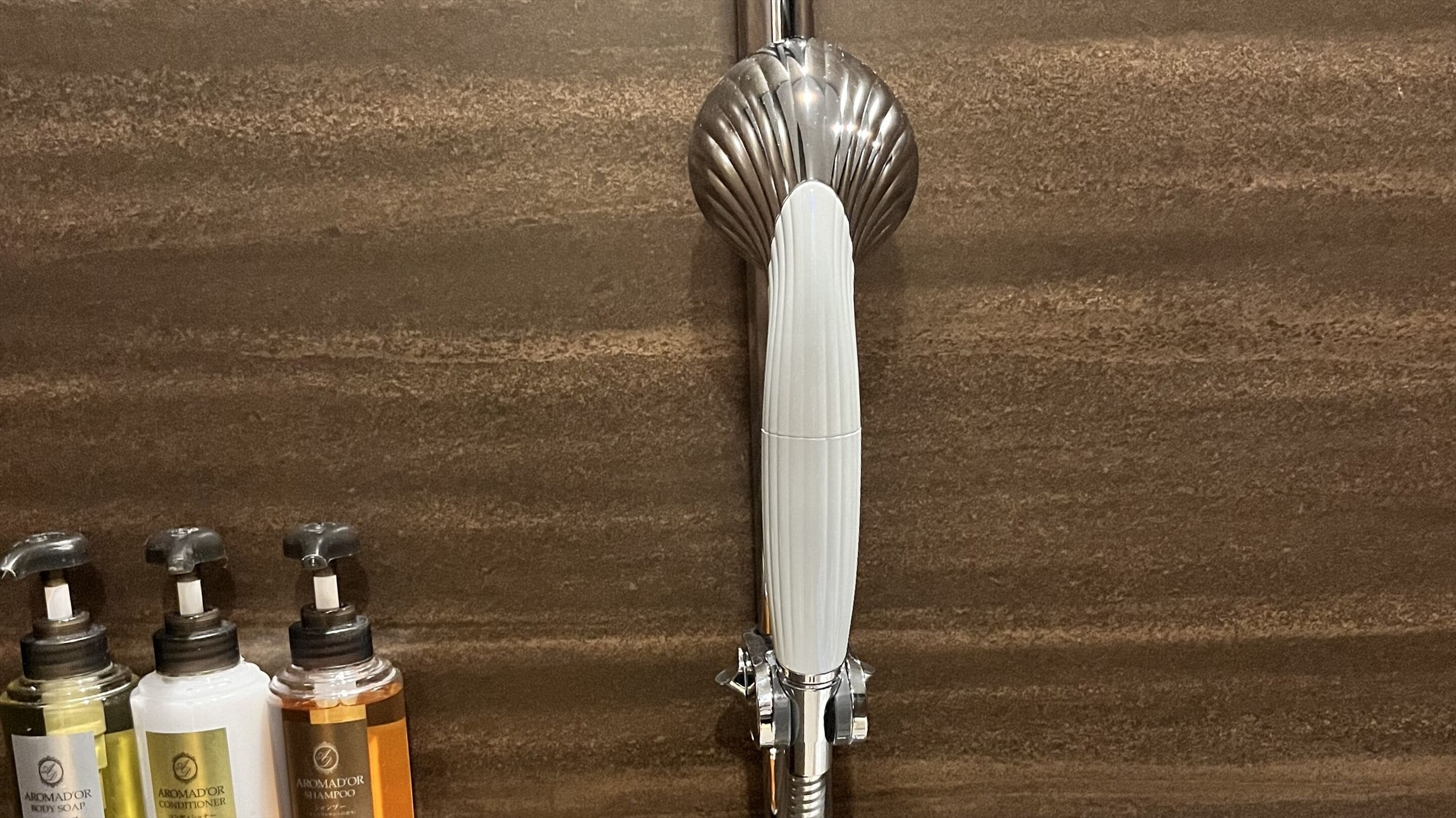 A shower with a modern, metallic faucet and a wooden wall.