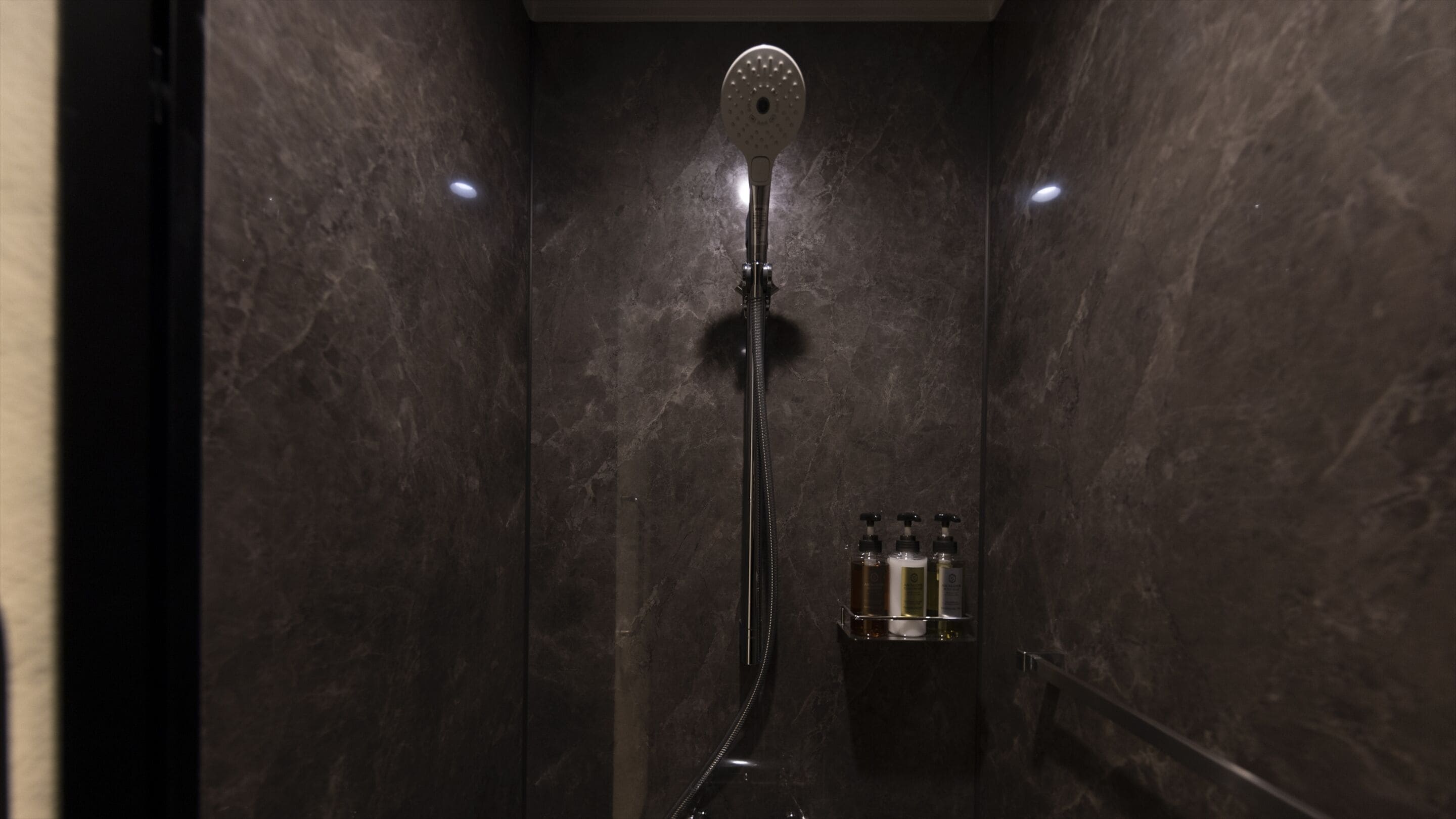 A modern shower with a handheld showerhead, a handheld shower attachment, and a bottle of shampoo.