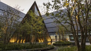 A modern building with a triangular glass facade, surrounded by trees and a water feature. - THE BLOSSOM KUMAMOTO (Kumamoto)