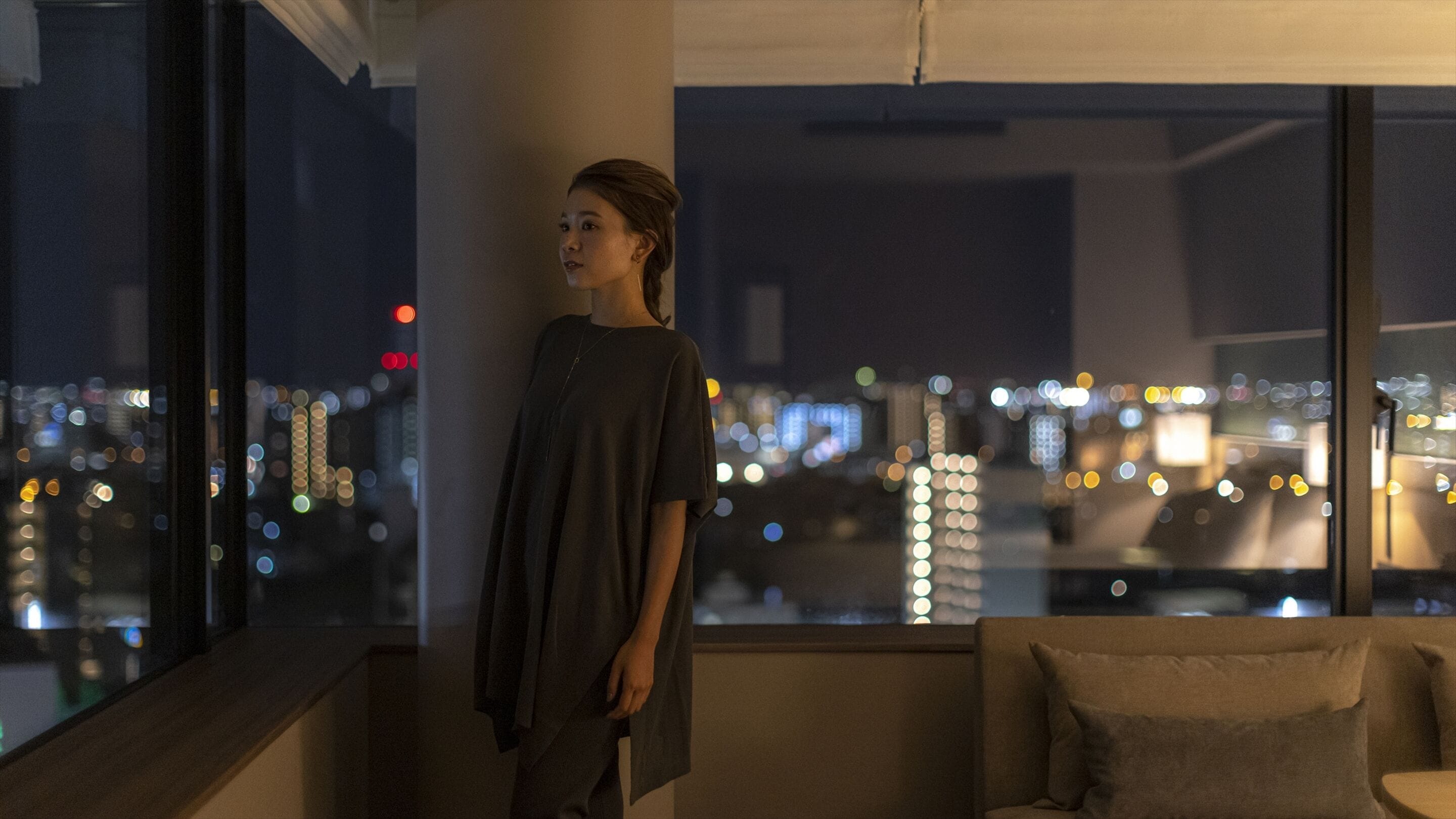 A person standing by a window overlooking a cityscape at night.