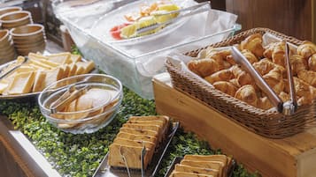 A buffet with various food items including bread, pastries, and a glass container with fruit.