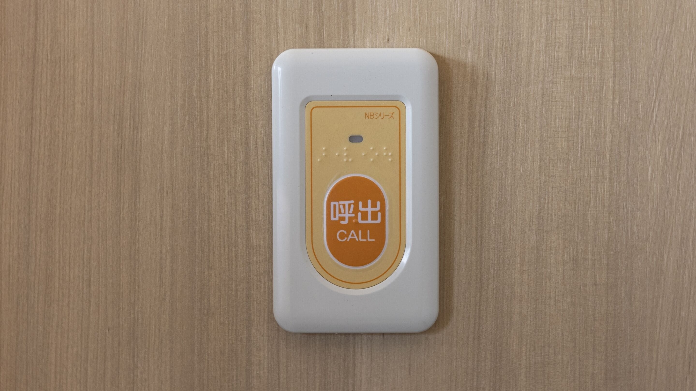 A white intercom with a call button on a wooden surface.