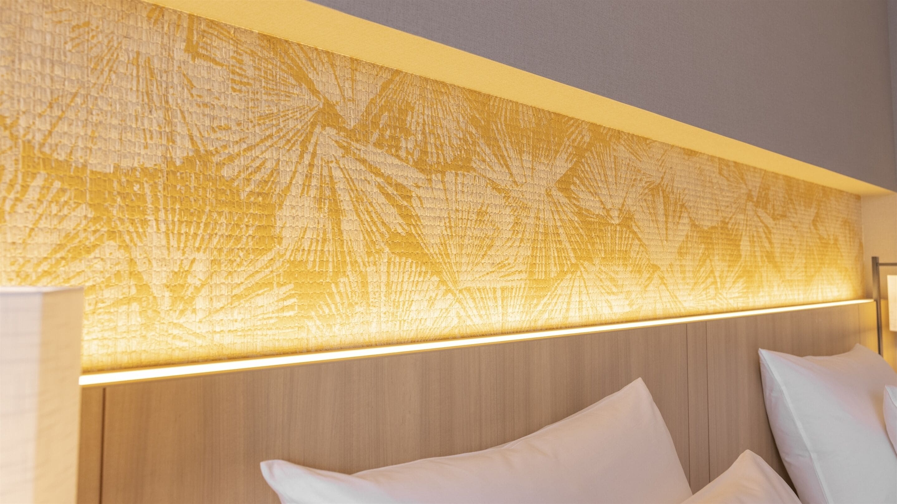A hotel room with a wooden headboard, a textured wall panel, and white bedding.