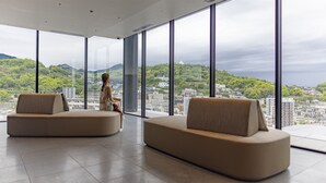 A spacious room with large windows offering a city view, two sofas, and a ceiling with recessed lighting. - THE BLOSSOM KUMAMOTO (Kumamoto)