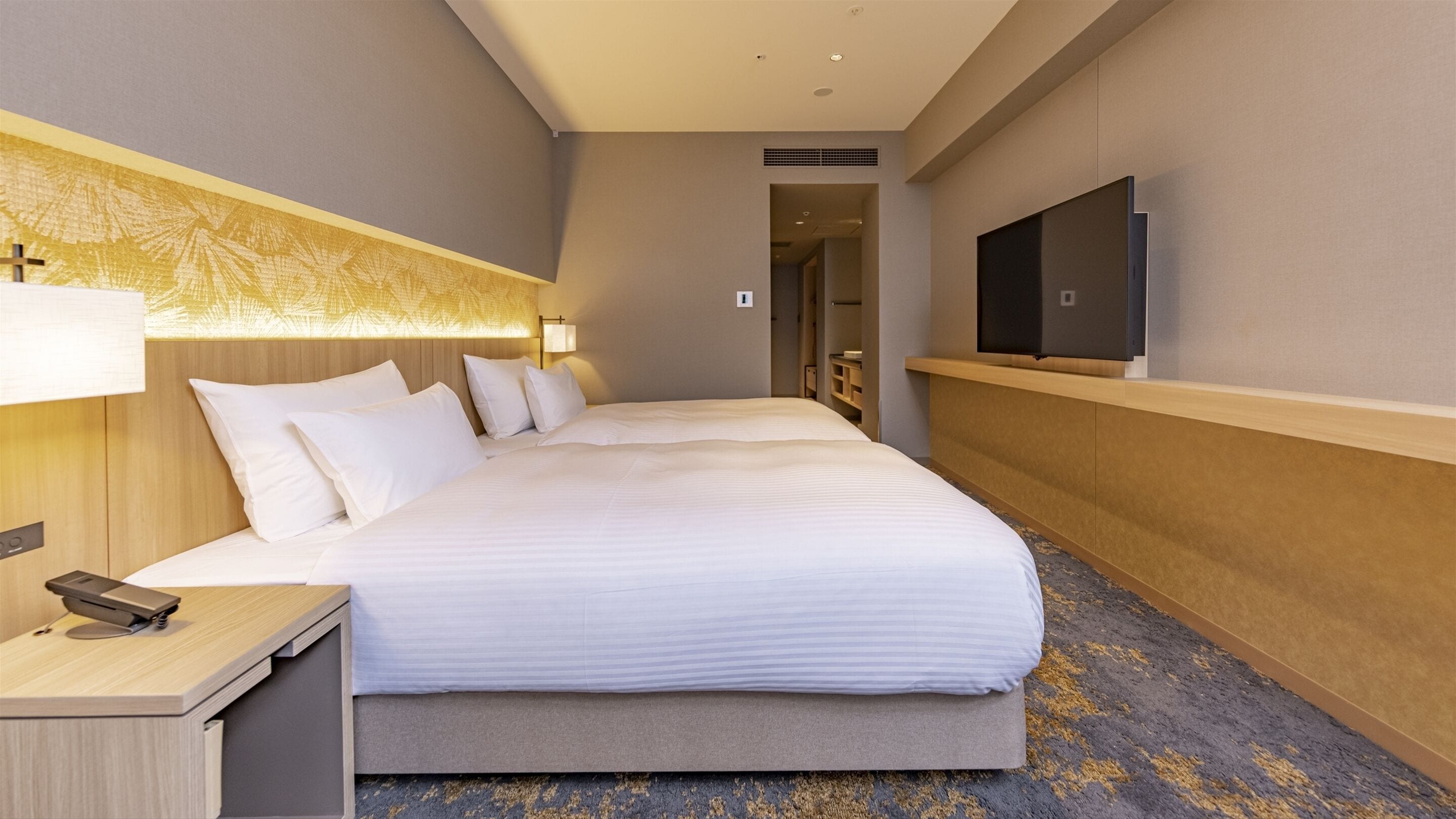 Une chambre d’hôtel avec un grand lit, une table de chevet avec un téléphone, un téléviseur fixé au mur et une tête de lit à motifs.