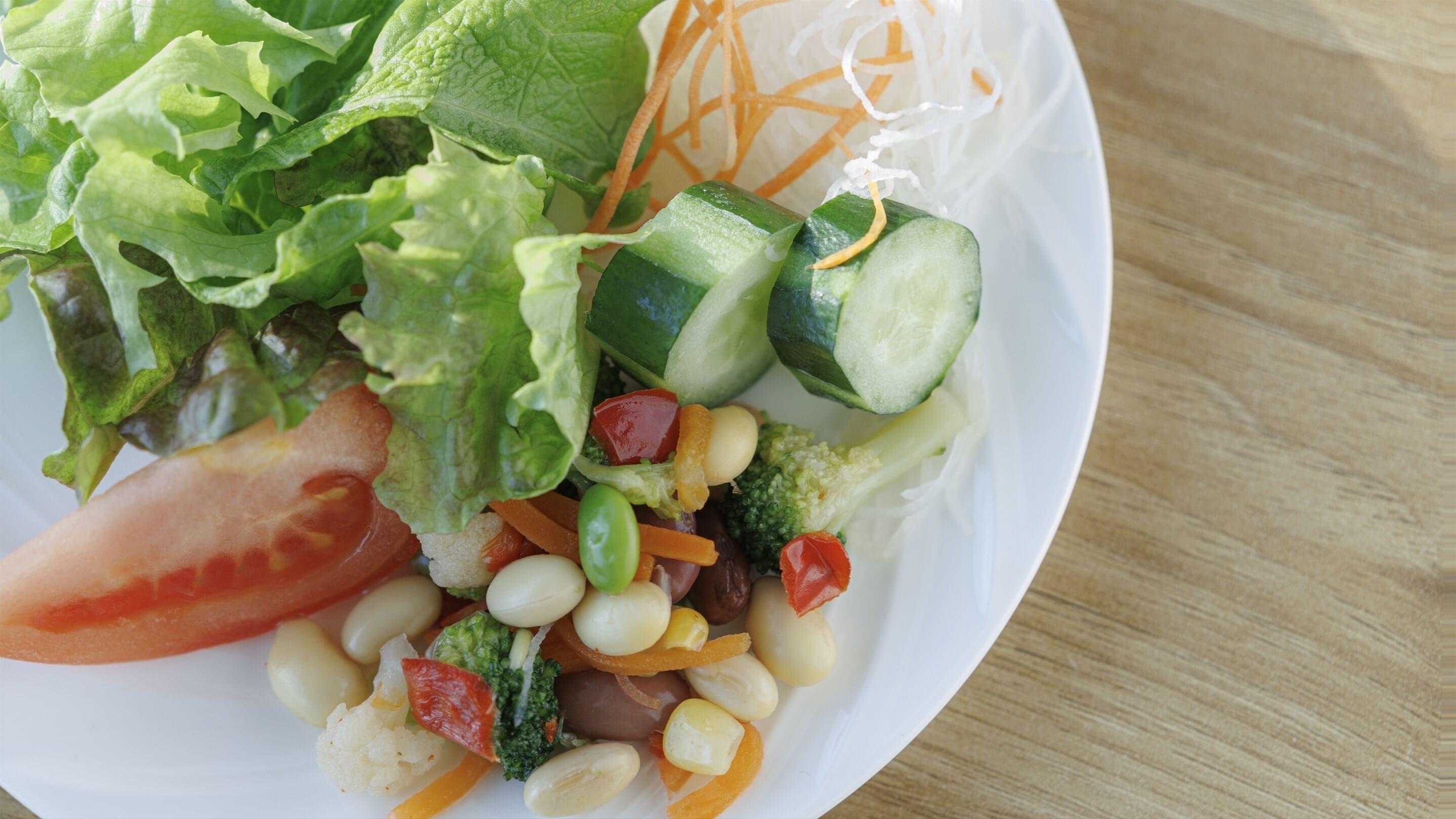 A plate of mixed vegetables including lettuce, tomatoes, cucumbers, broccoli, and carrots.