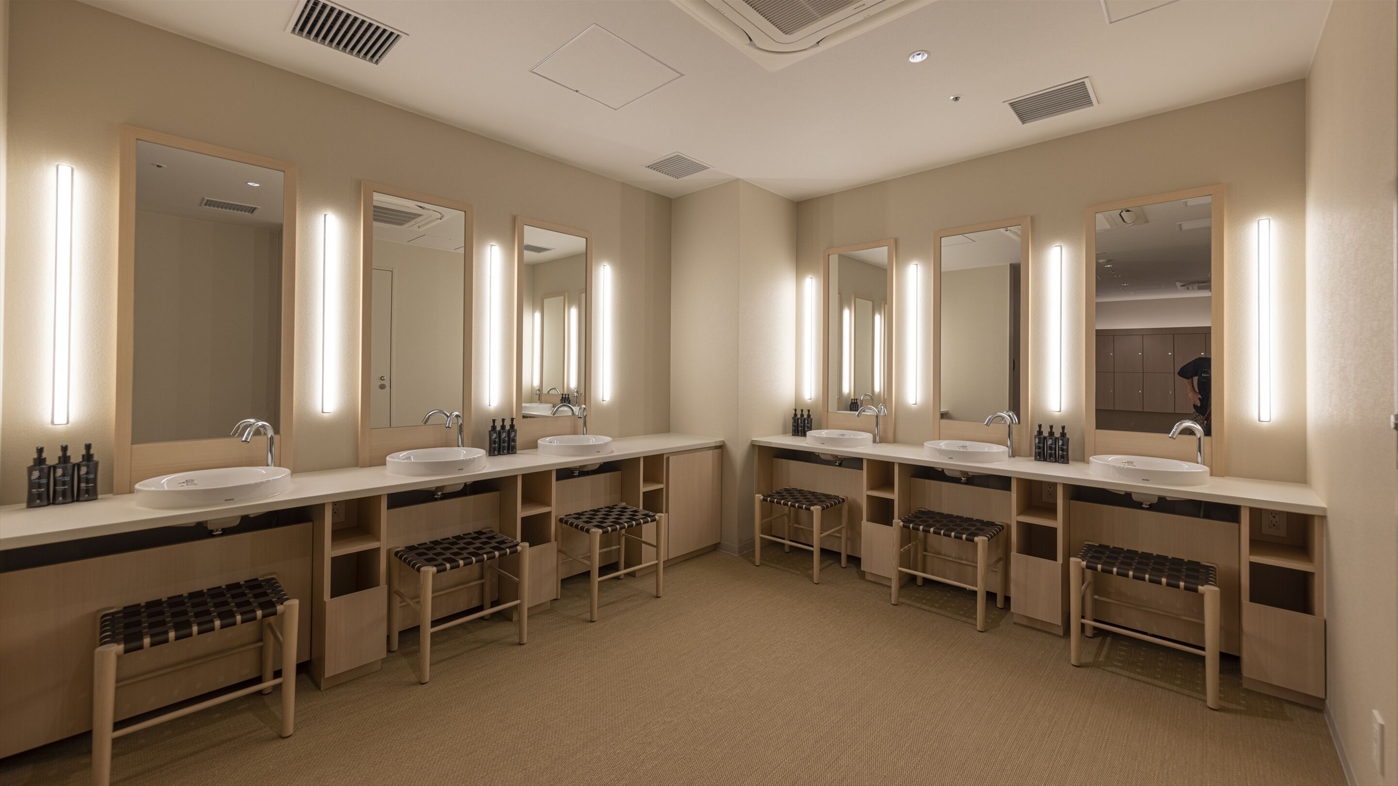 Un baño moderno con dos lavamanos, espejos amplios y bancos de madera.