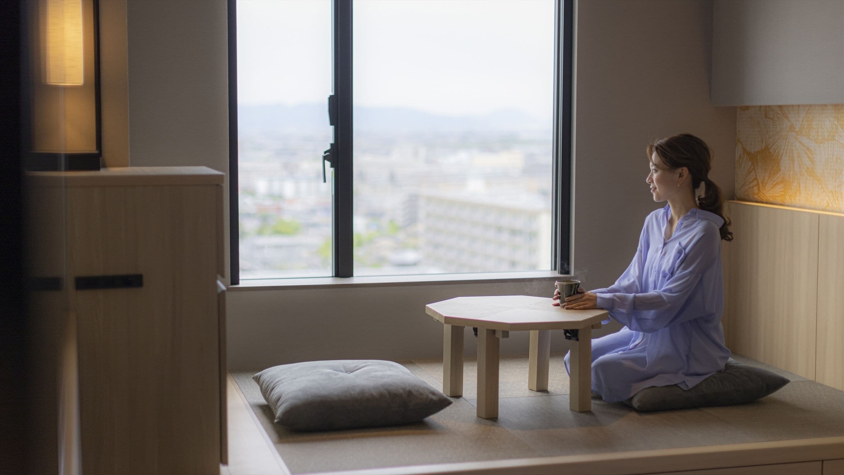 A person sitting on a bench by a window with a city view.