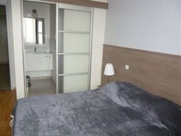 A bedroom with a bed, a nightstand, a lamp, and a wardrobe.