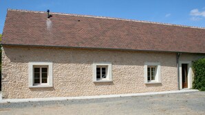 Un bâtiment en pierre avec un toit recouvert de tuiles, deux fenêtres et une porte.