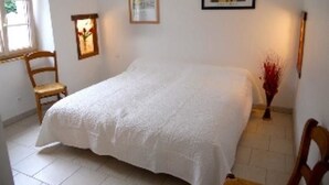 Une chambre à coucher avec un grand lit, une chaise, une fenêtre et deux tableaux encadrés accrochés au mur.