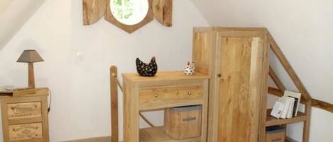 Een houten kast met lades en planken, een kleine tafel met een lamp, en een decoratief beeldje van een kip.
