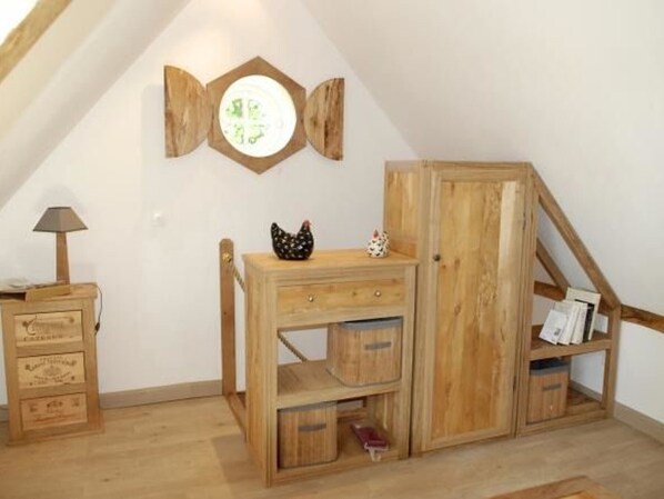Eine Holzkabine mit Schubladen und Regalen, ein kleiner Tisch mit Lampe sowie eine dekorative Hühnerfigur.