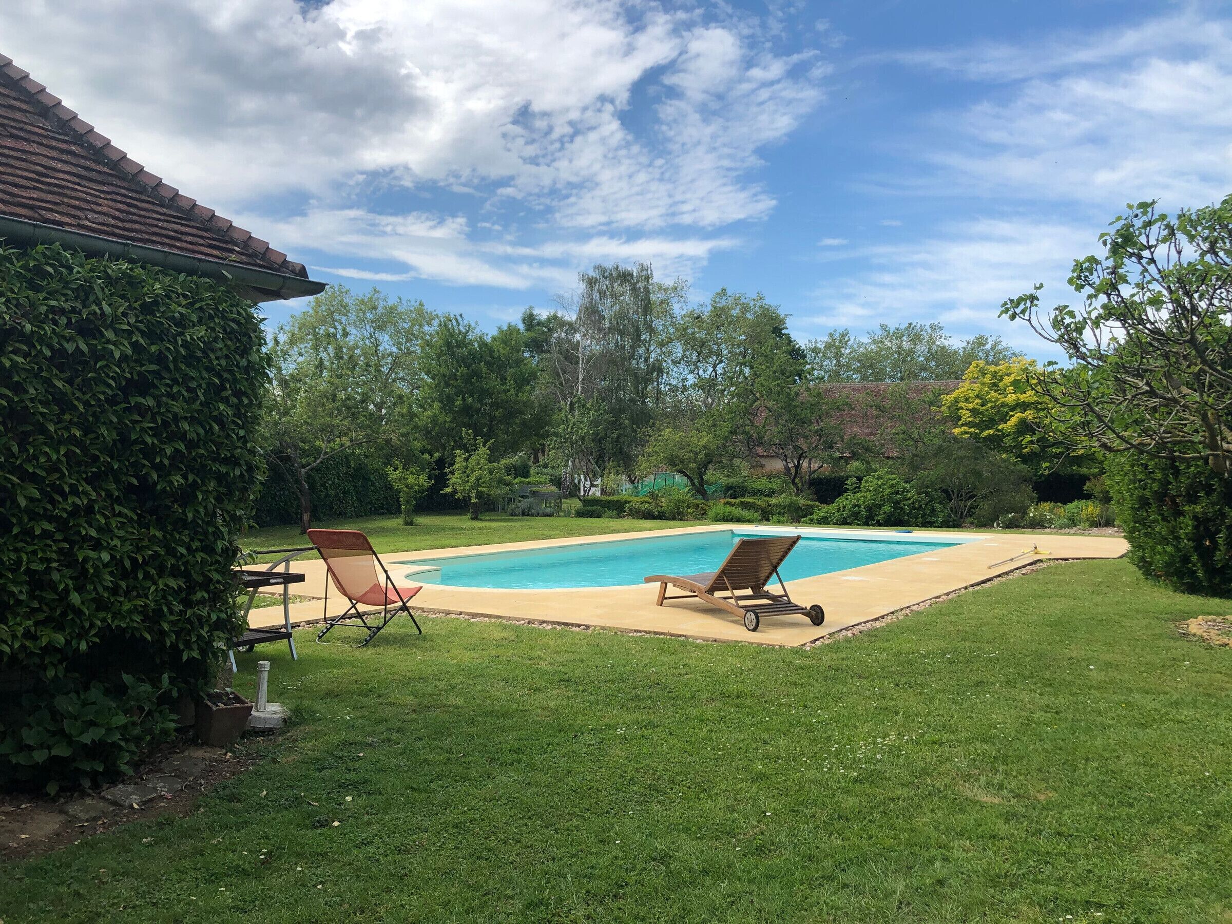 Un patio trasero con piscina, dos sillones de descanso y césped cuidado.