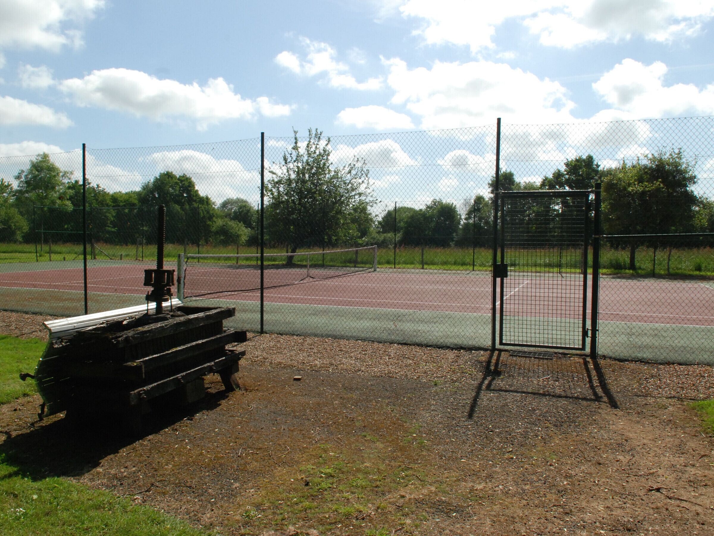 Een omheind tennisveld met een bankje en een poort.