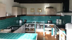 Een keuken met blauwgroene tegels, roestvrijstalen apparatuur en houten kastjes.