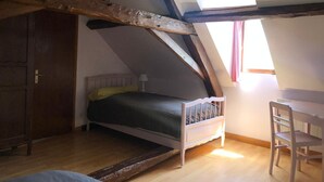 Een slaapkamer met een schuine kap, een bed, een bureau en een stoel.