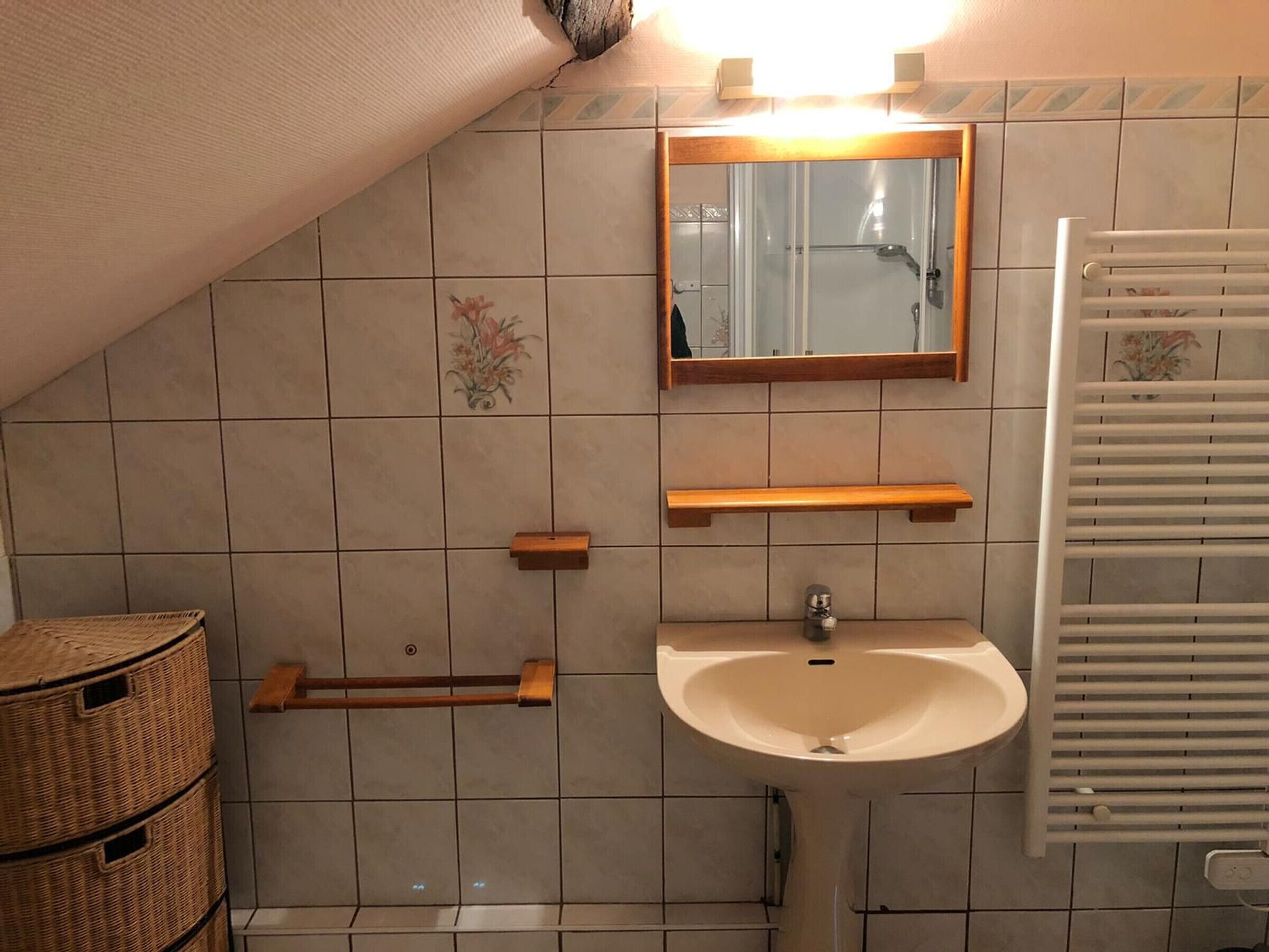 A bathroom with a white sink, a mirror, and a towel rack. There are wicker baskets and a shower area visible.