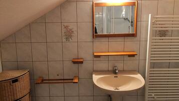 A bathroom with a white sink, a mirror, and a towel rack. There are wicker baskets and a shower area visible.
