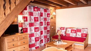 Una habitación acogedora con un aparador de madera, un sofá rojo, una mesa de madera y una cortina estampada.